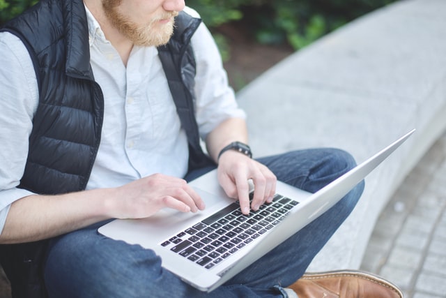 a man sitting on a stone bench using a laptop