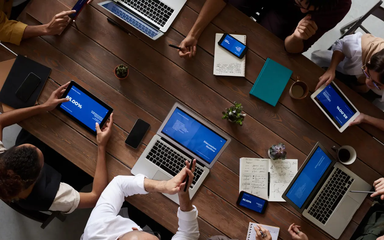a group of people sitting around a table with laptops and tablets