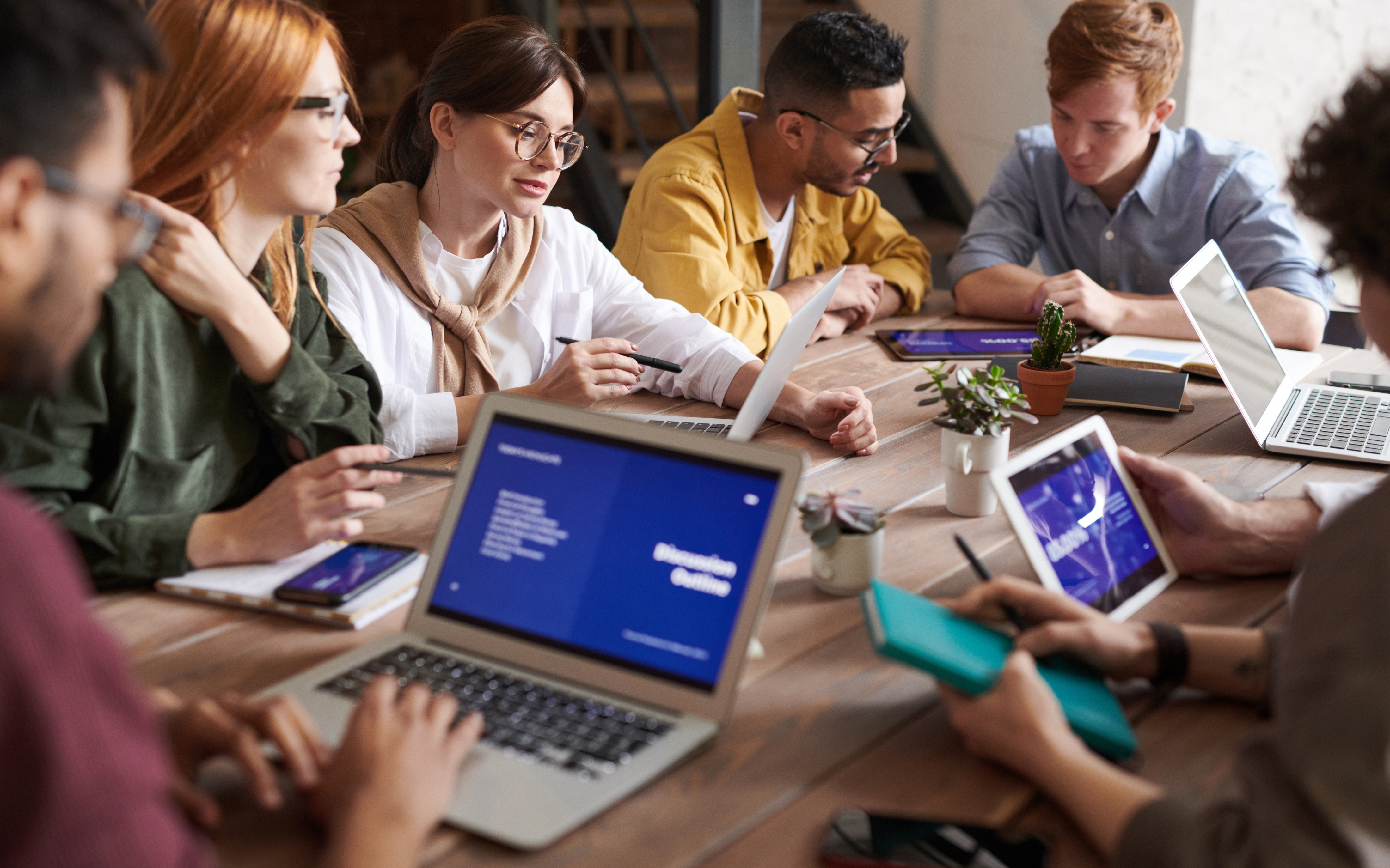 a group of people sitting around a table with laptops