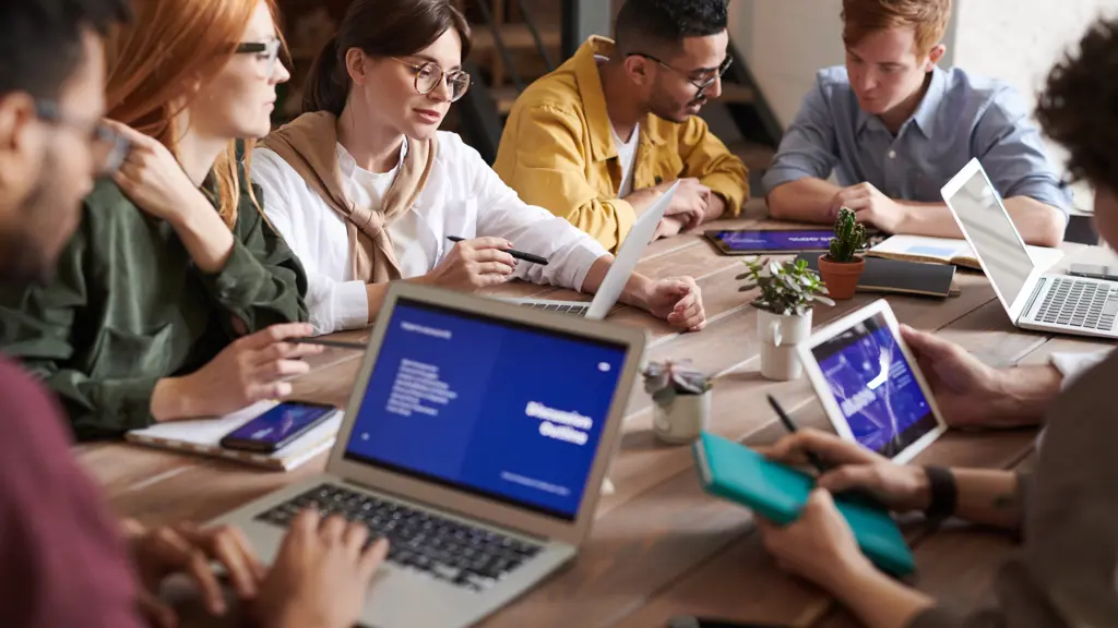 a group of people sitting around a table with laptops