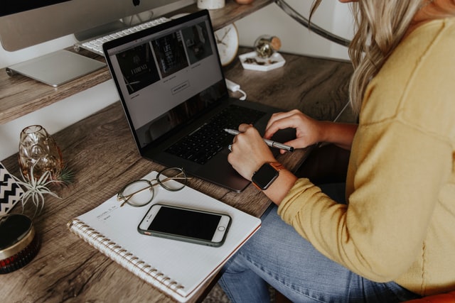 a woman sitting at a desk using a laptop and a phone