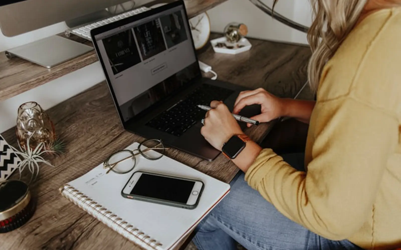 a woman sitting at a desk using a laptop and a phone